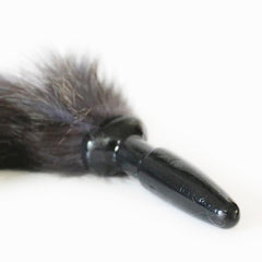 Black and white image of a person holding the anal plug with fox tail, demonstrating its size and shape